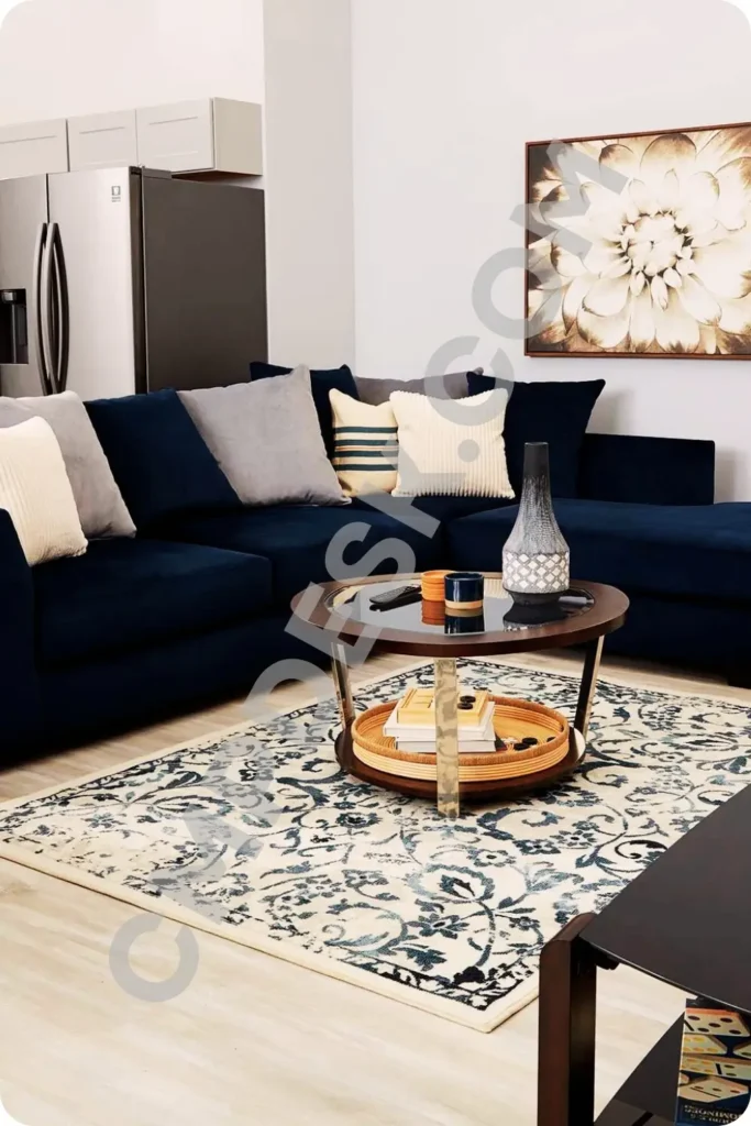 A cozy living room layout anchored by a floral-patterned blue and cream area rug beneath a navy blue sectional sofa and a round glass-top coffee table.